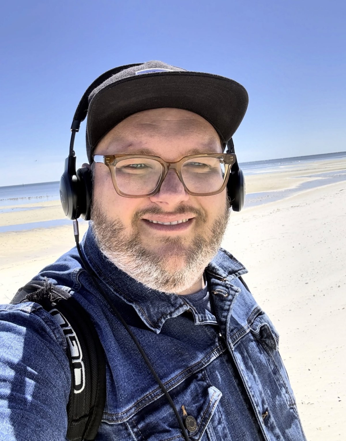 Jeff Allen on a beach wearing headphones and a denim jacket